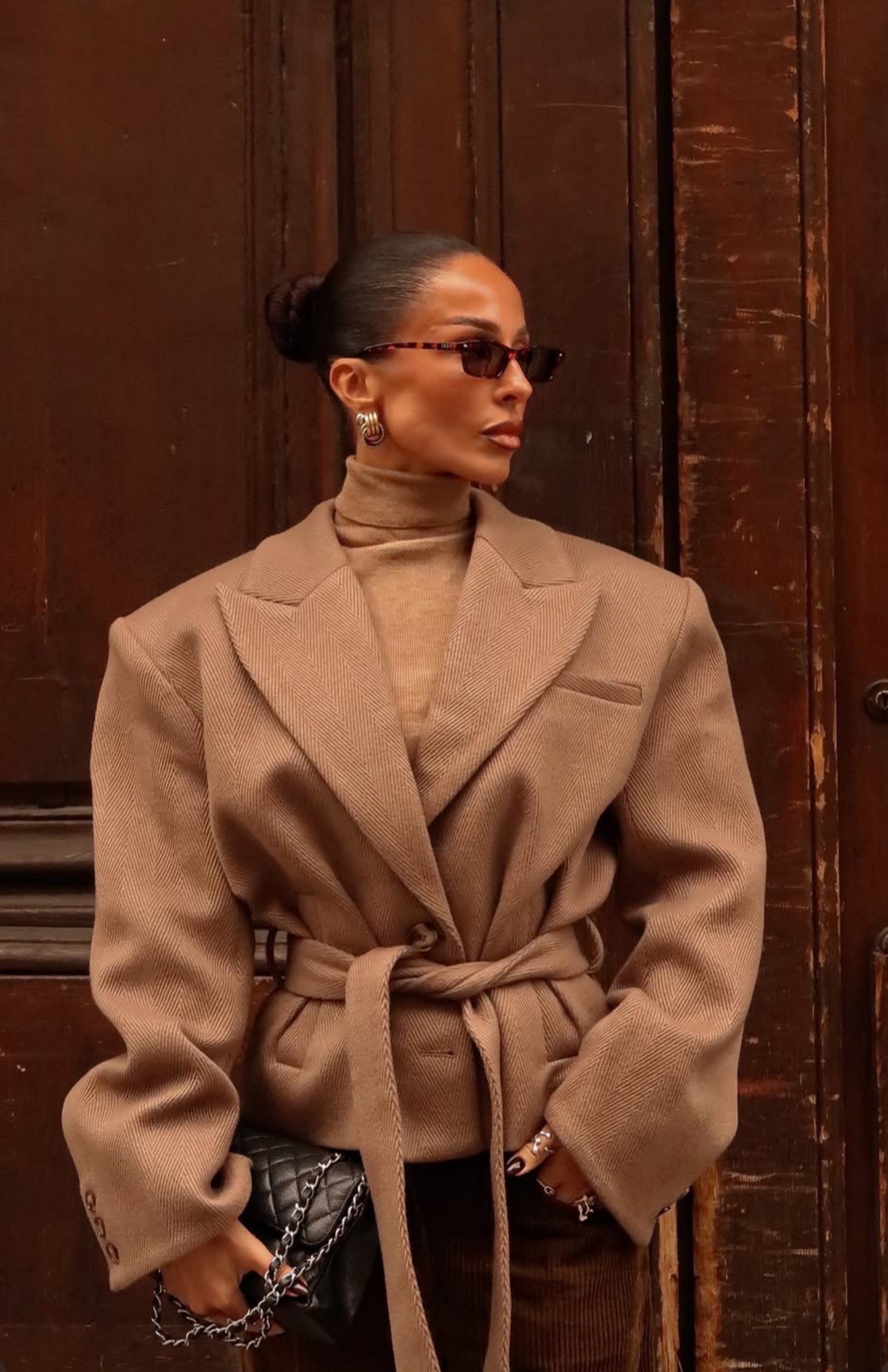 Woman wearing a beige coat and turtleneck against a wooden door.