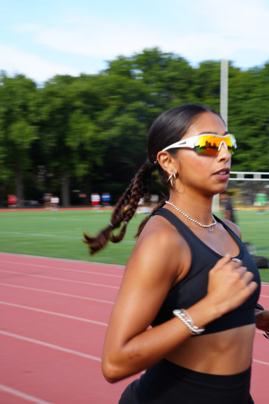 Woman wearing Indy sport sunglasses on a track field with trees in the background