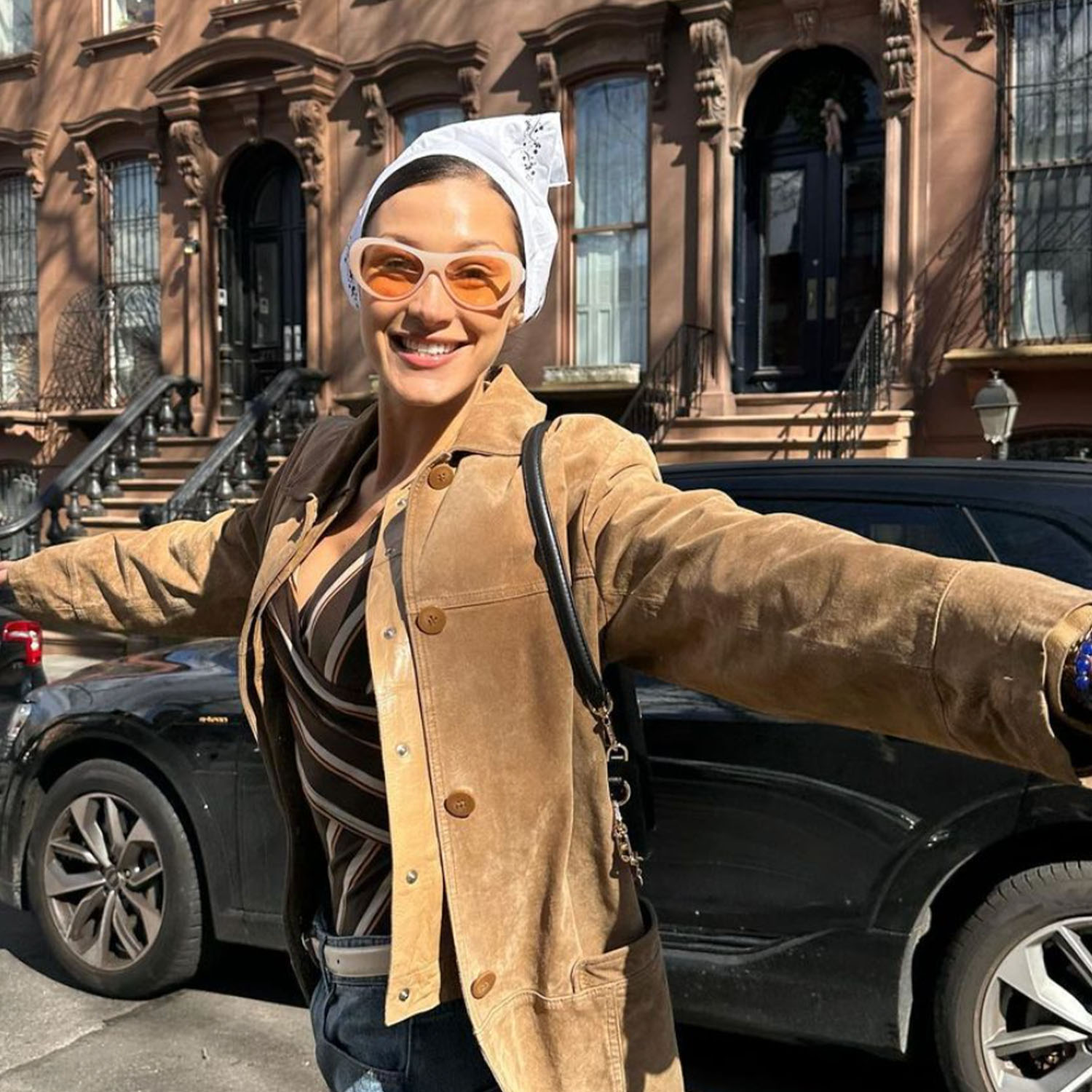 Bella Hadid wearing sunglasses and a brown jacket