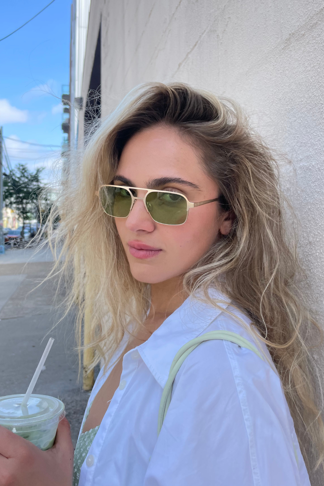 Woman with sunglasses and a drink against a light-colored wall