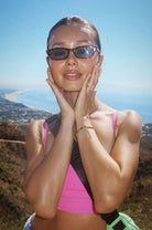 Woman wearing blue sunglasses and a pink top with a scenic background